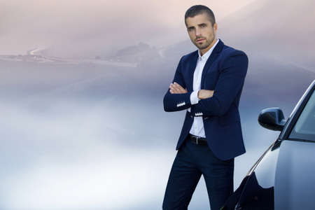 Successful, handsome man near a car on the side of a mountain roadの写真素材