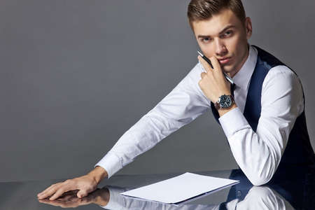 A man in a suit at a writing desk with a pen isolated on a gray background, studio.