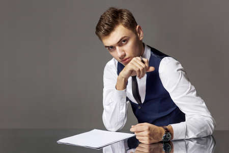 A man in a suit at a writing desk with a pen isolated on a gray background, studio.の写真素材