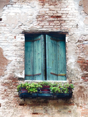 An old window with shutters and flowers in pots in the stone wall of a residential building.の写真素材