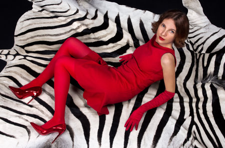 A girl in a red dress, shoes and tights lies on a zebra skinの写真素材
