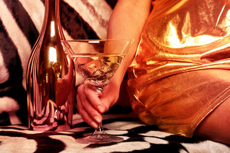 Beautiful woman drinks a cocktail on a rich background. Female hand with a martini on the background of a shiny bottle and a zebra skin.の写真素材