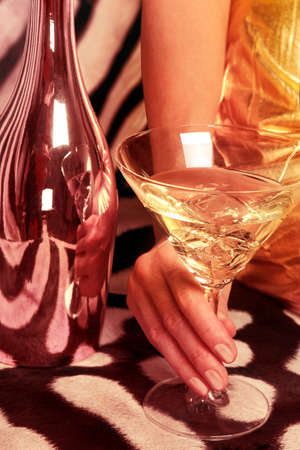 Beautiful woman drinks a cocktail on a rich background. Female hand with a martini on the background of a shiny bottle and a zebra skin.の写真素材