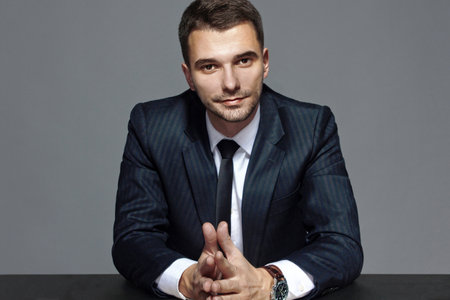 Portrait of a business man in formal suit at the table, isolated on gray background, studio.の写真素材