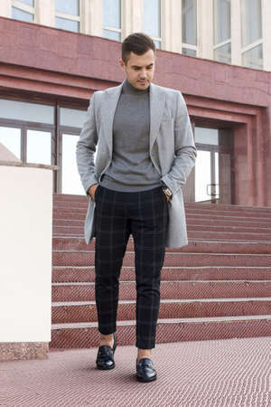 Handsome young man in gray autumn coat stands on the steps of a buildingの写真素材