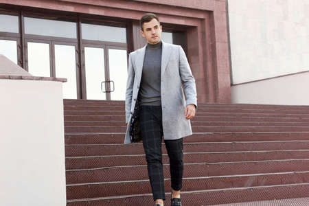 Handsome young man in gray autumn coat goes down the steps of the buildingの写真素材