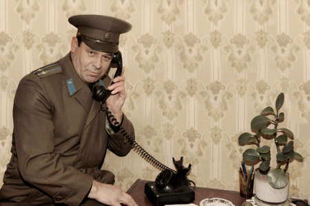 Portrait of a man in the form of a Soviet officer with a telephone receiver, talking on an landline phone.の写真素材