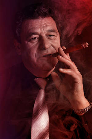 Handsome mature man smoking a cigar in a club, close-up portrait.の写真素材