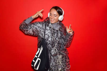 girl in fashionable clothes and headphones is cheerful on a red background.の写真素材
