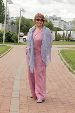 Mature plus size woman walks in the park in overalls in summer, trendy set of clothes. Urban summer fashion.の写真素材