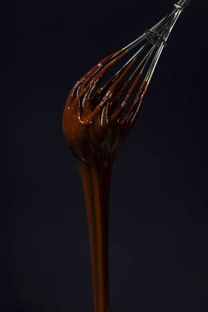 Chocolate is whipped with a whisk. Close-up of a wire whisk and melted chocolate on a black...