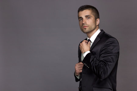 A respectable man in a strict black suit straightens his tie with his hand.の写真素材