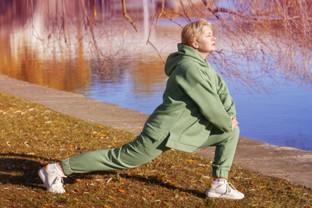 Mature woman in a green fleece hoodie doing stretching in the autumn park. healthy lifestyle.の写真素材