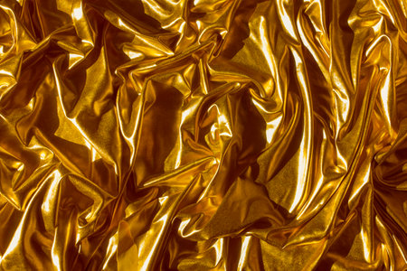 Golden wavy abstract background. Background of luxurious fabric, wavy folds, satin shiny material or draperyの写真素材