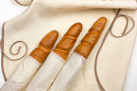 Crispy baguette wrapped in white paper lies on a linen tableclothの写真素材