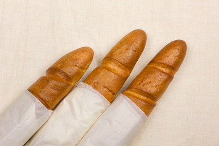 Crispy baguette wrapped in white paper lies on a linen tableclothの写真素材