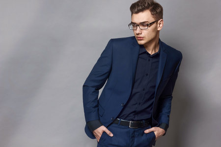 Portrait of an elegant handsome businessman in glasses, blue classic suit, on a gray background with copy space.の写真素材