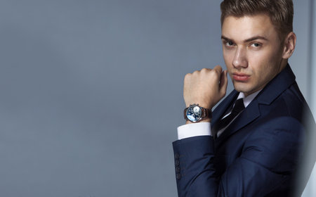 man in an expensive suit in a tie and an expensive watch posing on a gray background with copy spaceの写真素材
