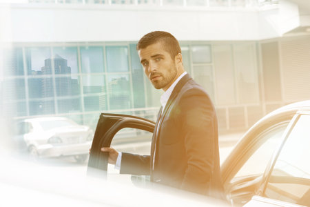 A middle-aged man stands next to a car in the city in the morning, the sun is rising.の写真素材