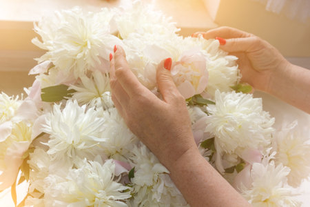 Female hands with bright red manicure on white peoniesの写真素材
