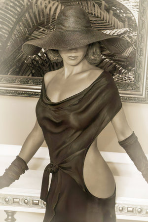 A girl in a big black hat and black gloves in front of a painting with palm leaves. Fashion, beauty.の写真素材