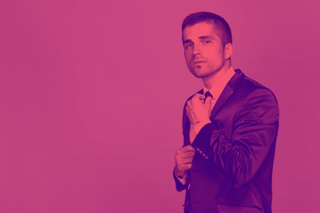 A toned pink photograph is a half-length portrait of a handsome man in a black suit and tie with a slight stubble.の写真素材