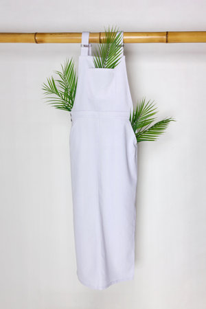 Long white jumpsuit hanging on a white background on an eco-friendly bamboo hanger.の写真素材