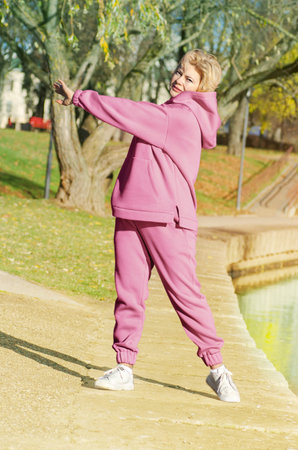 Mature woman in pink hoodie doing sports in autumn park.の写真素材