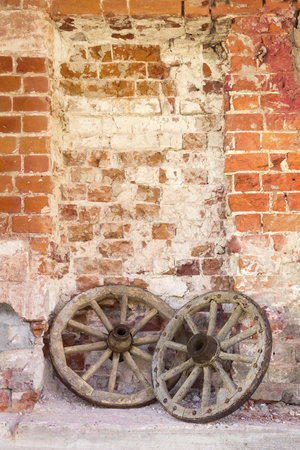 Wooden wheels from an old cart lie against the background of an old brick wall. Retro background.の写真素材