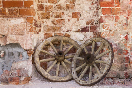 Wooden wheels from an old cart lie against the background of an old brick wall. Retro background.の写真素材