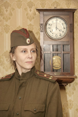 A woman in a military uniform against the background of old paper wallpaper and a clock with a pendulum. Vintage styling.の写真素材