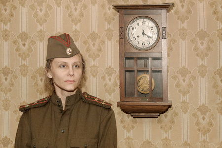 A woman in a military uniform against the background of old paper wallpaper and a clock with a pendulum. Vintage styling.の写真素材