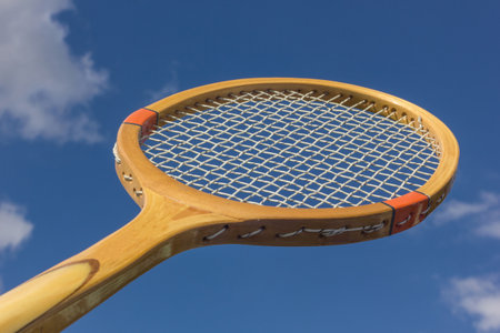 Sport wooden retro tennis racket on sky background outdoors. Wooden racket close up.の写真素材