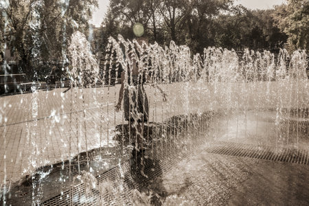 Children in a fountain in summer. Silhouette of a girl playing in the spray of a fountain.の写真素材