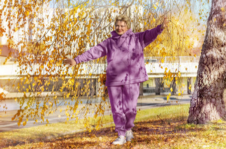 Mature woman in pink hoodie or tracksuit walking in autumn park. Digital detox, sport.の写真素材
