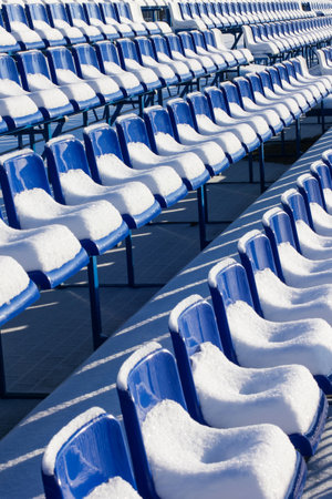 Winter stadium stands covered with snow. Stadium seats under snow, blue chairs under snow in winter.の写真素材