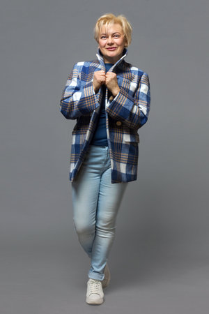 Mature woman in a plaid jacket, (large plaid), posing in the studio on a gray background. Fashion, modern classics.の写真素材