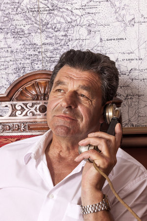 A man holding an important public position sits at a desk in his retro-elite office. He talks on the phone. Emotional conversation, portrait, close-up.の写真素材