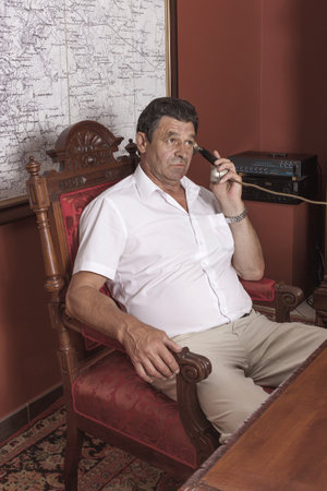 A man holding an important public position sits at a desk in his retro-elite office. He talks on the phone. Emotional conversation, portrait.の写真素材
