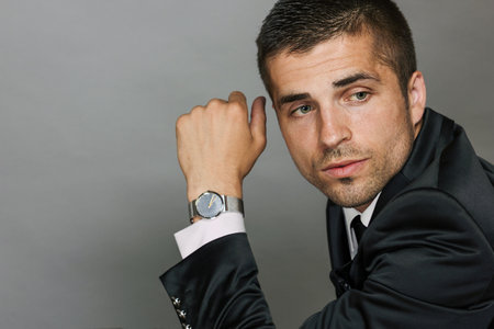 Close-up portrait of young man in elegant suit and white shirt on gray background. Male beauty, fashion. Wristwatch for successful man.の写真素材