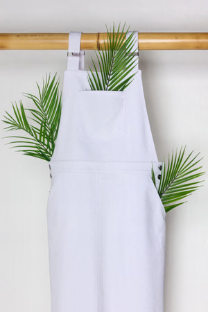 Long white jumpsuit hanging on a white background on an eco-friendly bamboo hanger.の写真素材