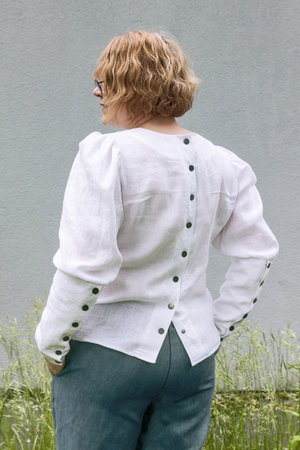 Mature woman in white linen blouse with puffy sleeves and long cuffs and metal buttons on the back posing. Back view, from behind, advertising, fashion.の写真素材