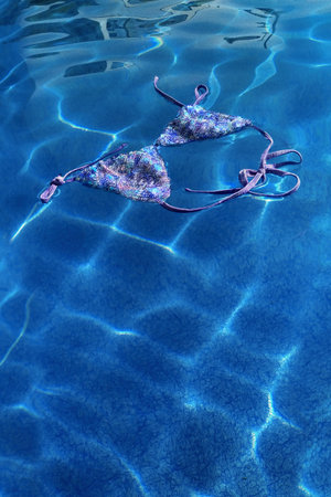 A colorful bikini drifts serenely on the surface of a sparkling blue pool, reflecting sunlight and...