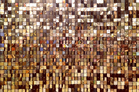 A decorative wall with an ornament of shiny mirrored gold and pink squares. The background is made of square mirrored tiles.の写真素材