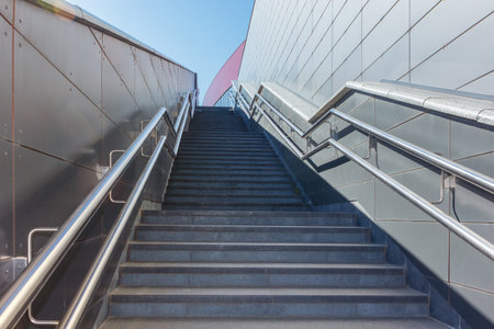 A modern staircase with smooth metal walls and sturdy silver handrails, the way up. Minimalistic...