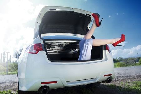Legs girl in red shoes visible from the trunk of a white car. Against the blue sky and grassの写真素材