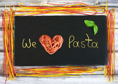 We love pasta, writing made from pasta arranged on a slate, horizontally, framed with linguineの写真素材