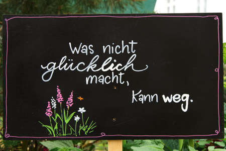 "What doesn't make you happy can go" written in white chalk on a black board, decorated with flowers, horizontallyの写真素材