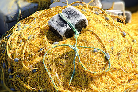 Yellow yarn fishing net with sinkers and large stone weight, horizontal