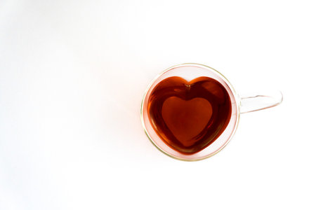 Heart-shaped glass teacup filled with red tea on a white background, free space on the left, top view, horizontalの写真素材